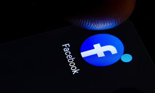 A finger about to tap a Facebook app icon on a dark screen.