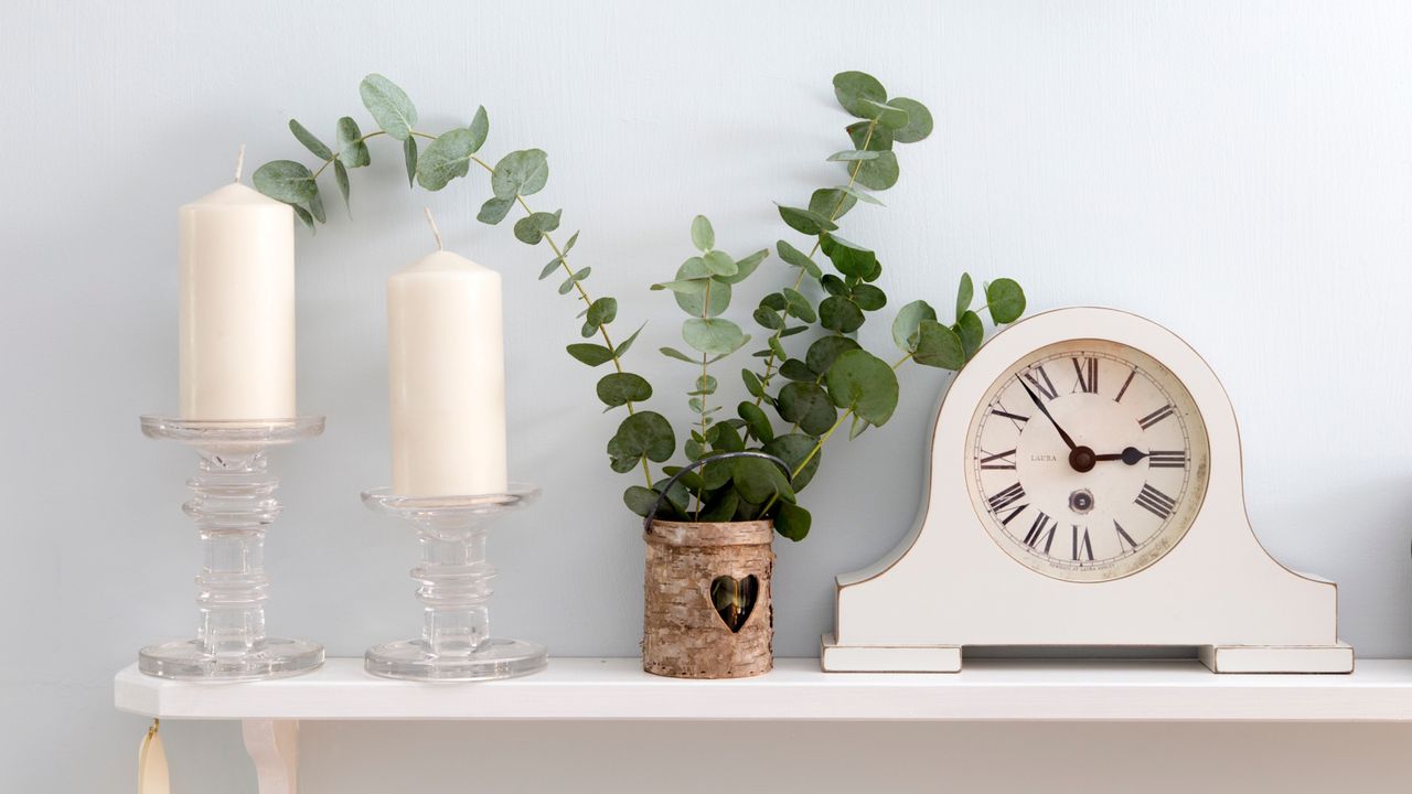 White mantlepiece clock next to plant and candles