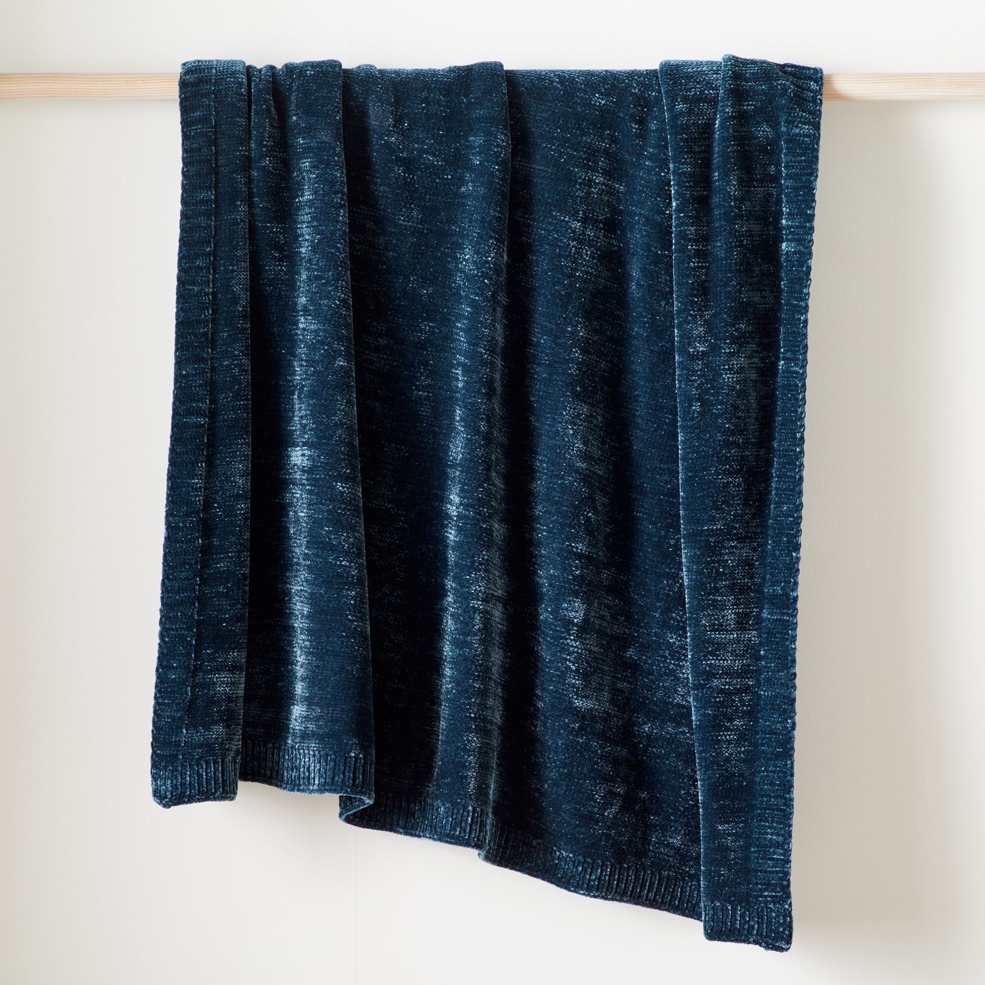 A dark blue West Elm chenille throw blanket on a rack