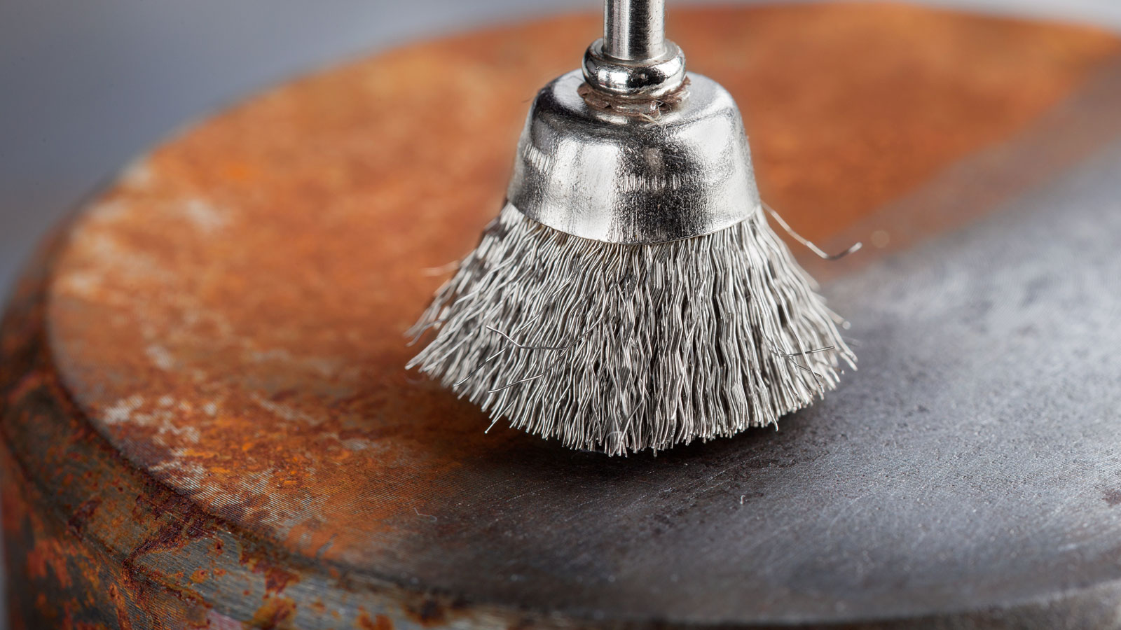 Steel wire brush wheel on top of metal surface with half rust and half cleaned