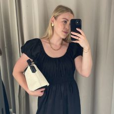 Woman wears black ruched dress and carries canvas cream and black tote bag