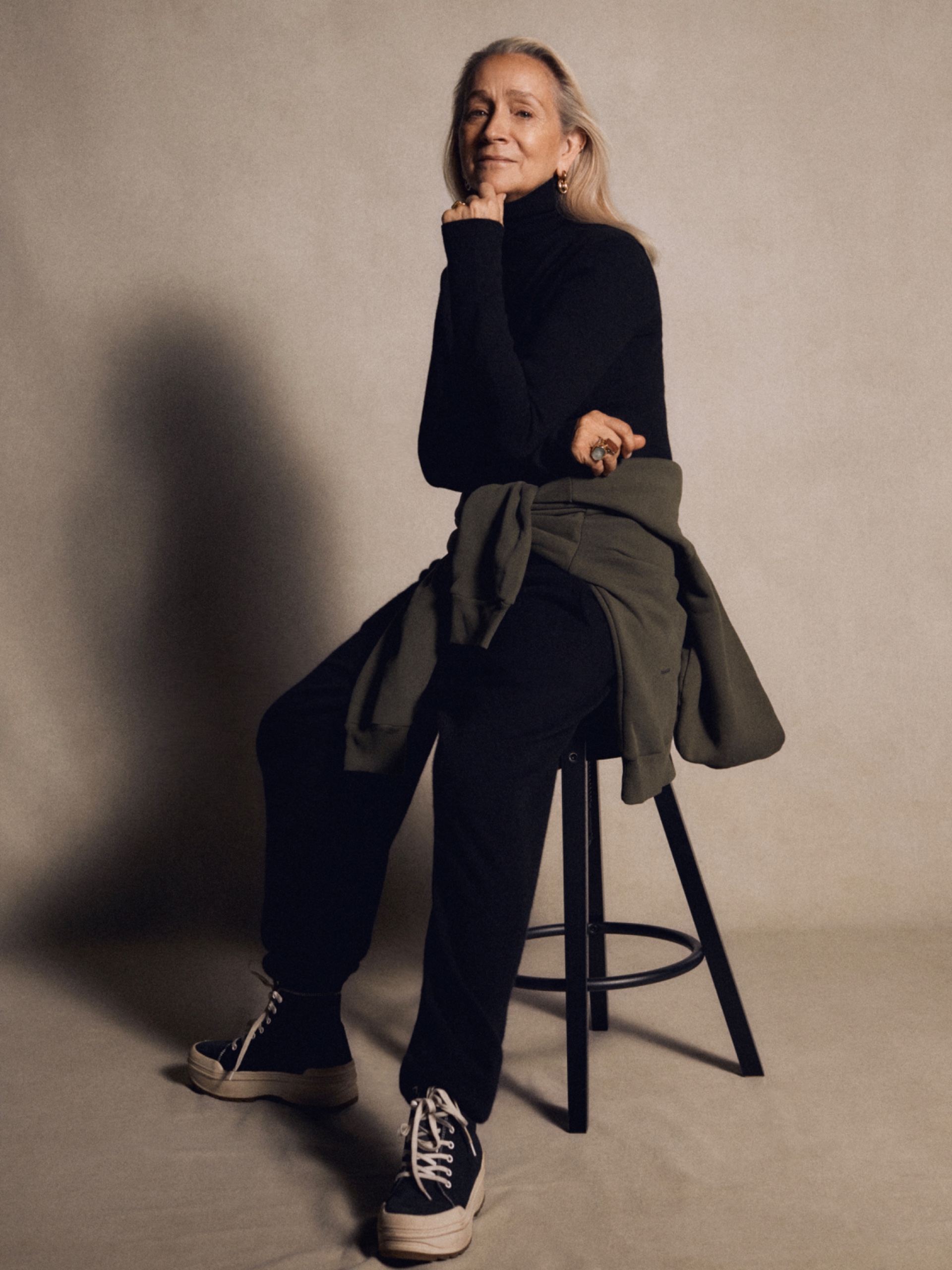 A woman wearing all black leaning on a stool, smiling at the camera
