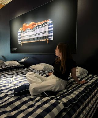 Emilia sitting on a Hästens mattress looking at a poster promoting spinal alignment.