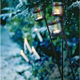 Wintry flower bed with stake glass and lanterns and outdoor candles