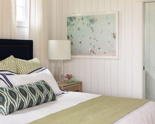 Coastal bedroom with white walls and pale green throw on bed and blue artwork