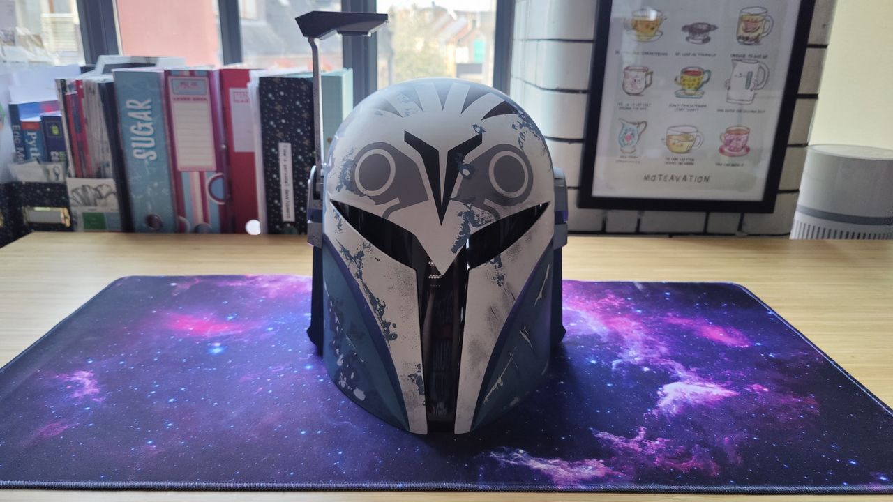 Black Series Bo-Katan Helmet with the heads-up display up. The helmet is facing forward. There is a gray, black, and white owl-like pattern on the light blue helmet and a black T-shaped visor.