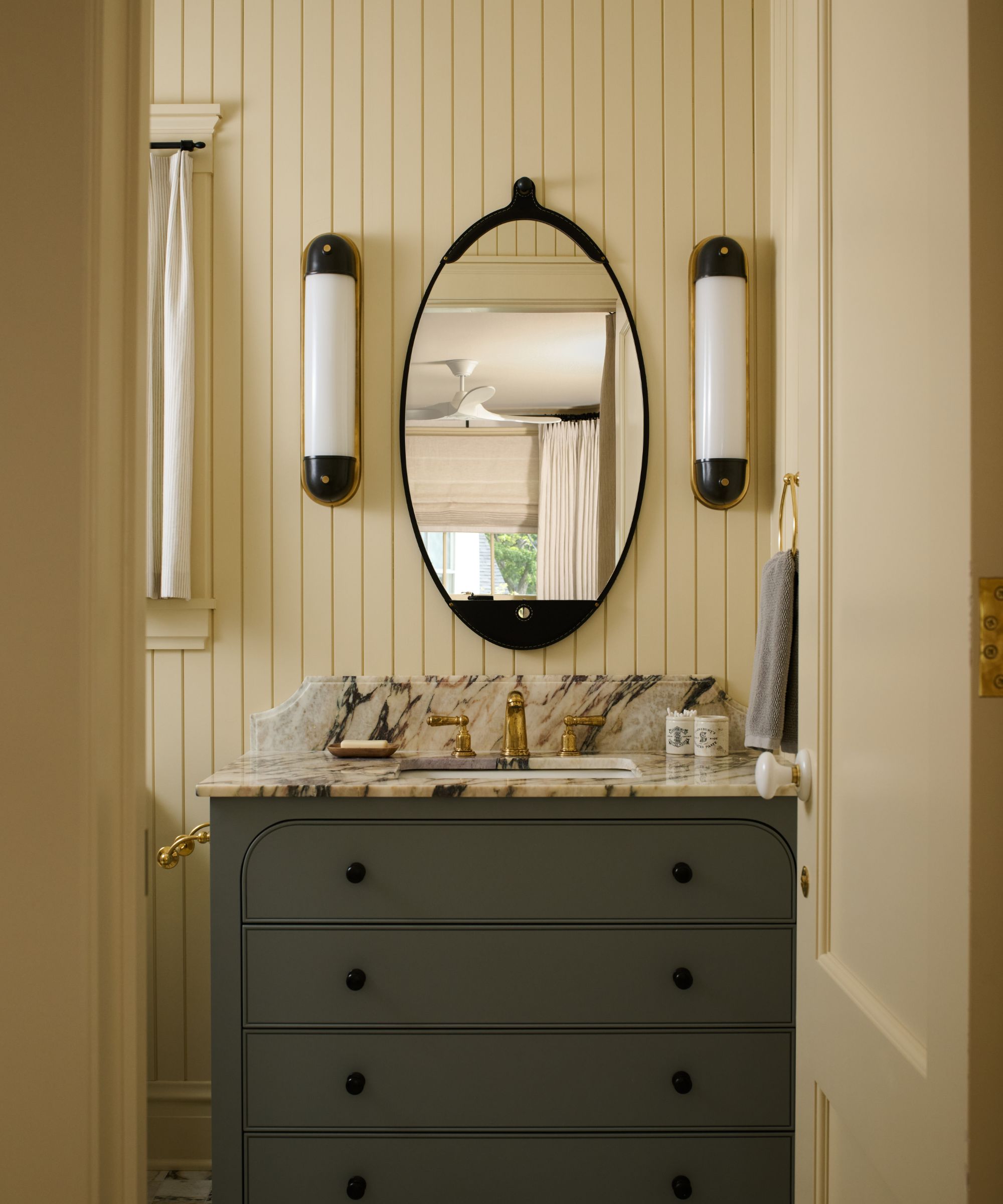 A butter yellow bathroom with wall panelling and a dark green cabinet with marble counters.