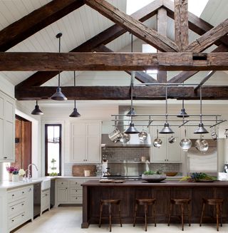 kitchen with white paneling and cabinets with dark wood island stools and beams and steel pot rack with multiple pendant lights