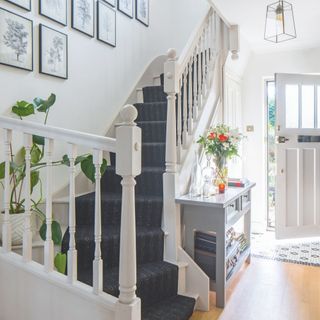 White hallway and staircase with blue runner on the stairs and a white front door partially open