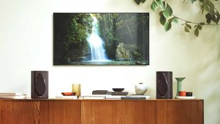 Sonus Faber Duettos on a tabletop in front of a wall-mounted TV