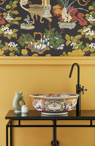 yellow bathroom with bold wallpaper, patterned basin, black vanity and tap