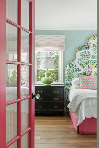 A bedroom with a pink door, a pink bed, and green accents