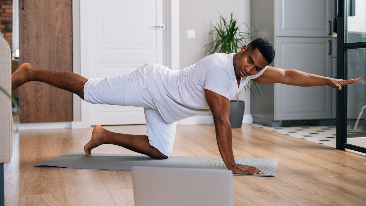 Man doing bird dog exercise at home watching laptop