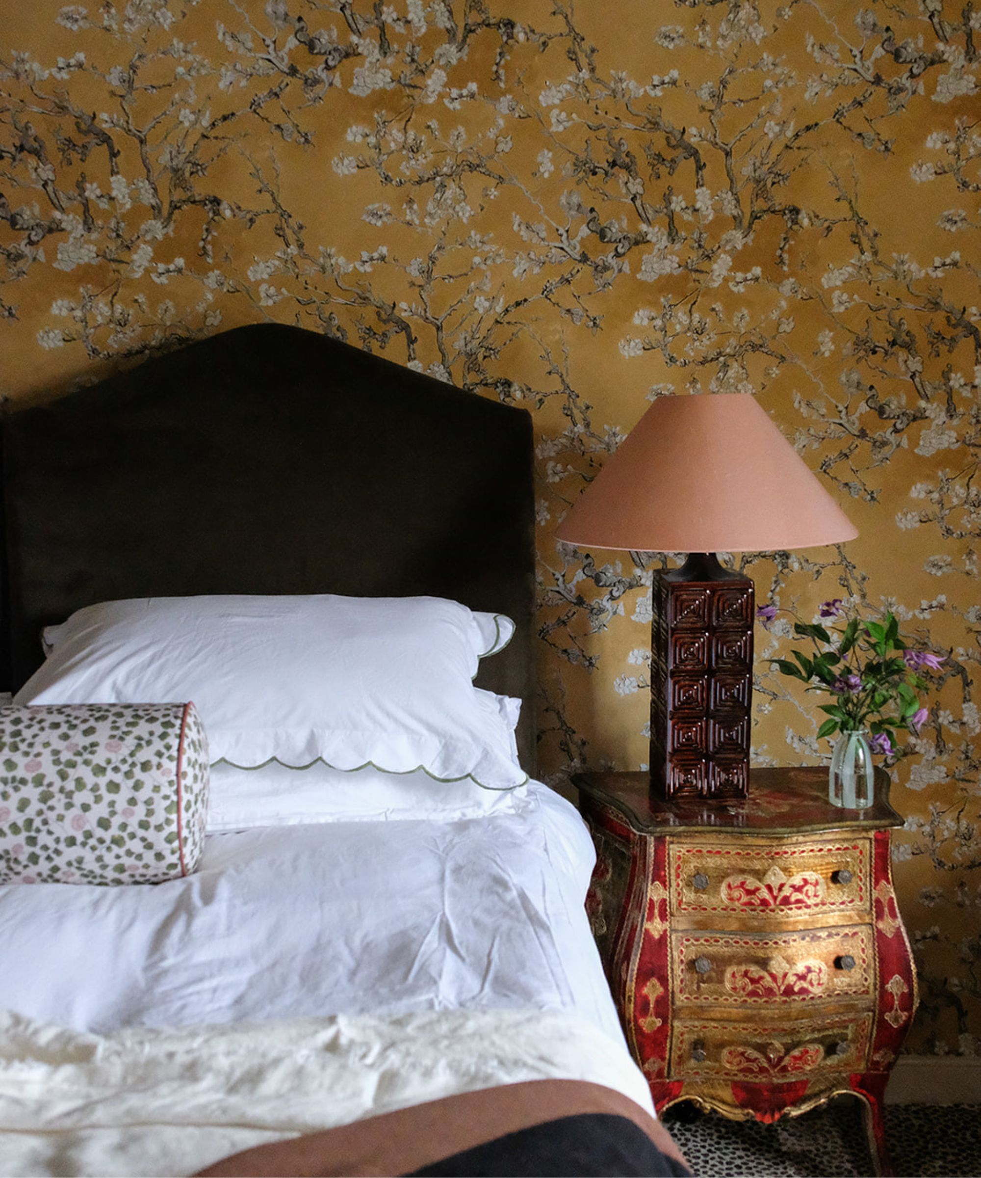 Bedroom with yellow floral wallpaper, single bed with white bedding, antique side table in gold with lamp and vase