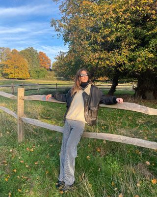  @camillecharriere wearing a black leather jacket, cream sweater, and striped cargo pants in a field.