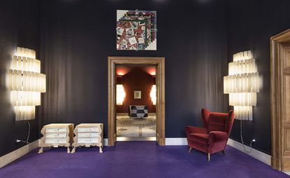 Gallery room with two large, multi-layered lights, velvet armchair and artwork above the door