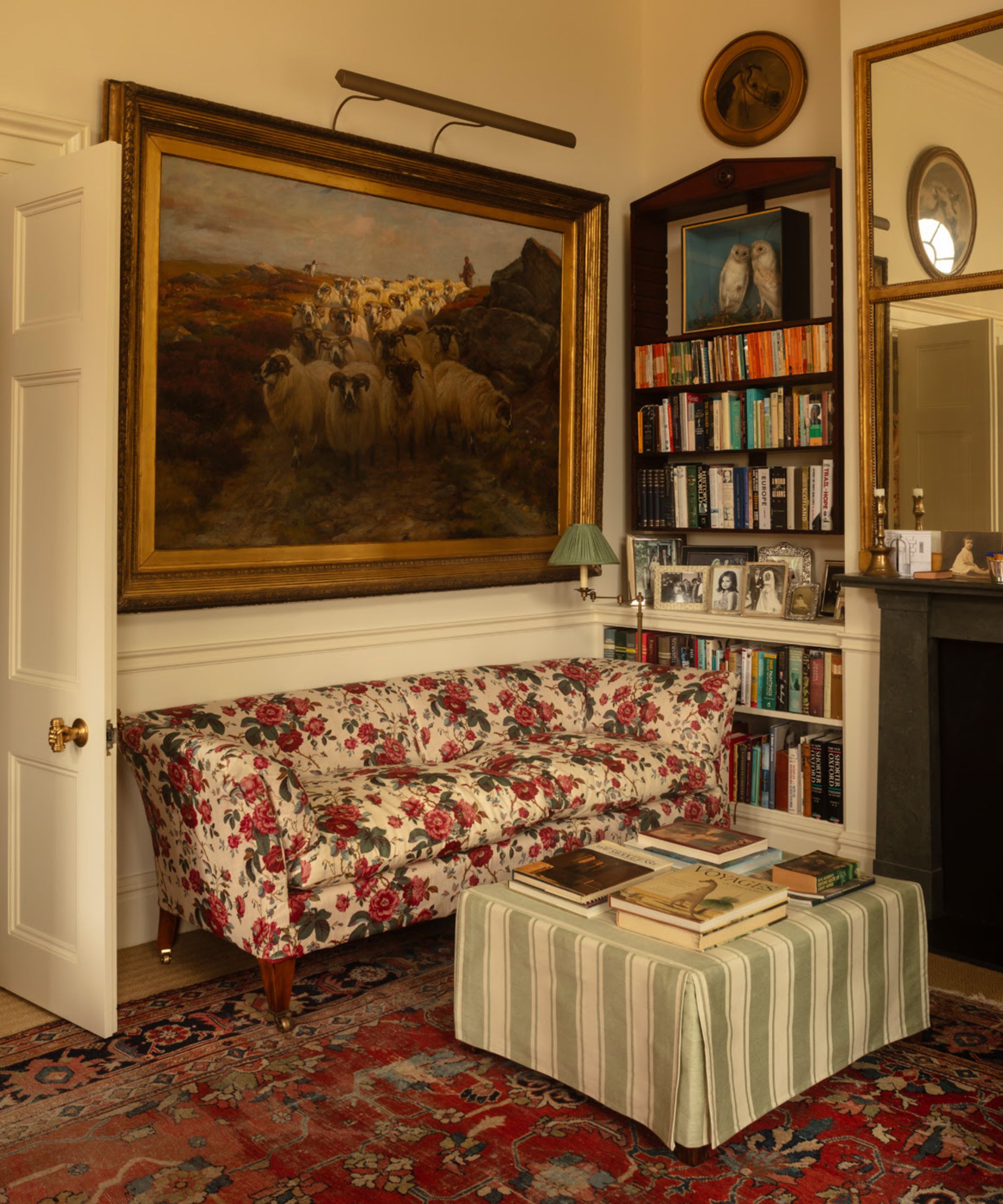 Cozy corner of a living room with floral sofa, striped ottoman, artwork on wall