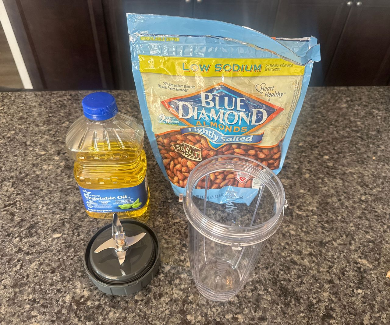 A bag of almonds, a bottle of oil, and a blending cup on a kitchen counter.