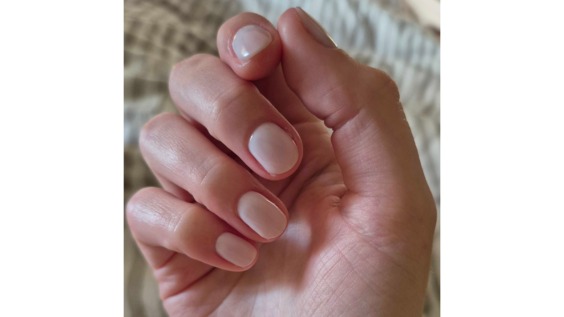 A close-up of Digital Beauty Writer, Naomi Jamieson's hand, pictured with short, milky white nails, in front of a striped bedding background