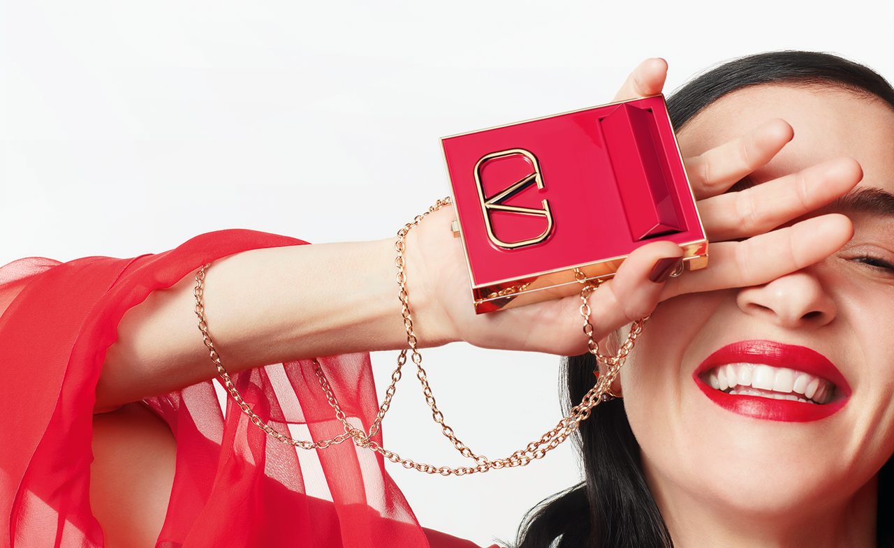 Model wearing Valentino Beauty red lipstick in red dress and holding Valentino Beauty compact