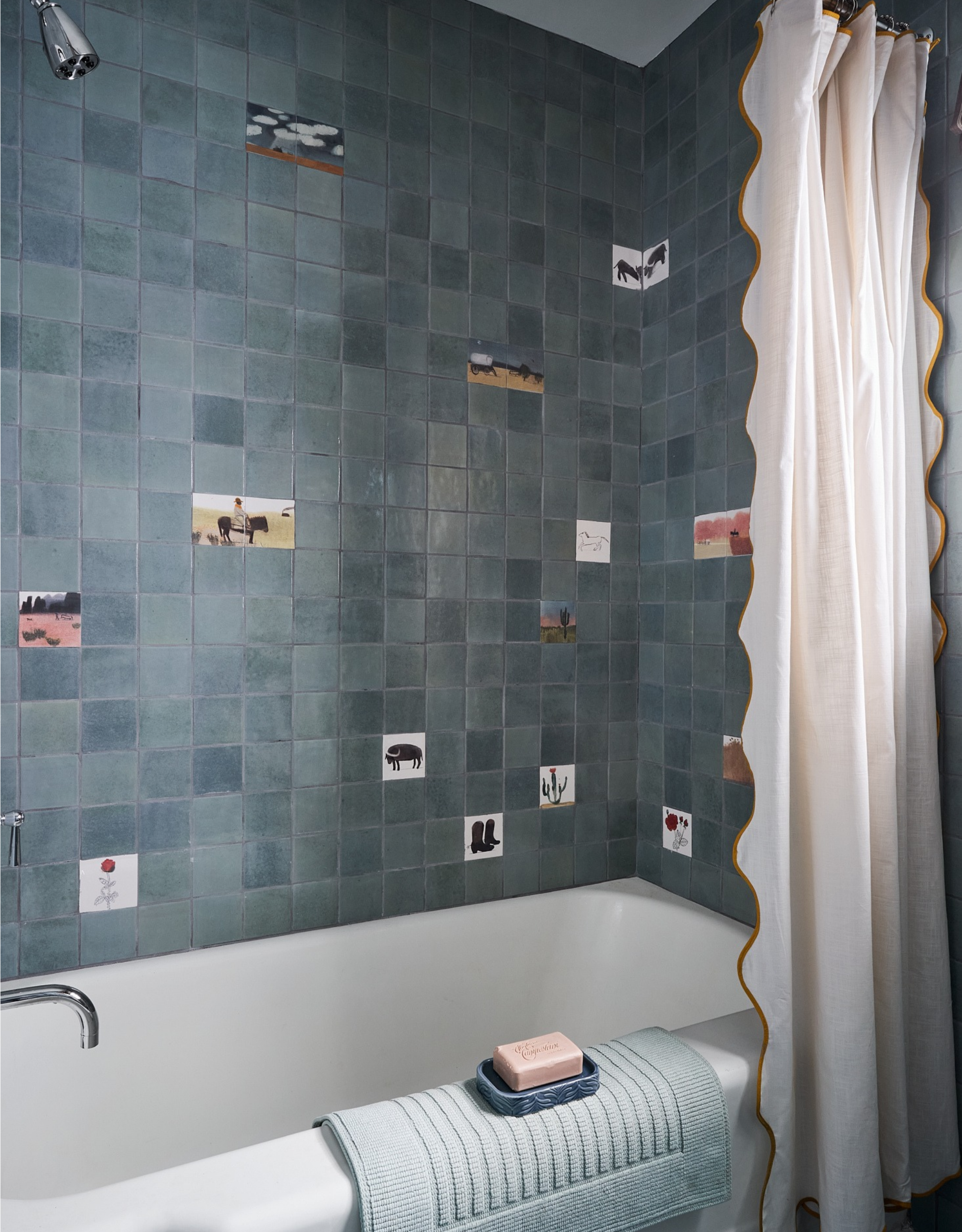 childrens bathroom with built in tub and blue tiles, with some cowboy illustrated tiles dotted throughout