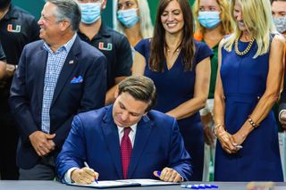 Ron DeSantis signing a bill at a desk with standing people behind him