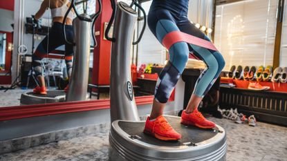 Lower half of woman's body using a Power Plate at the gym with resistance band