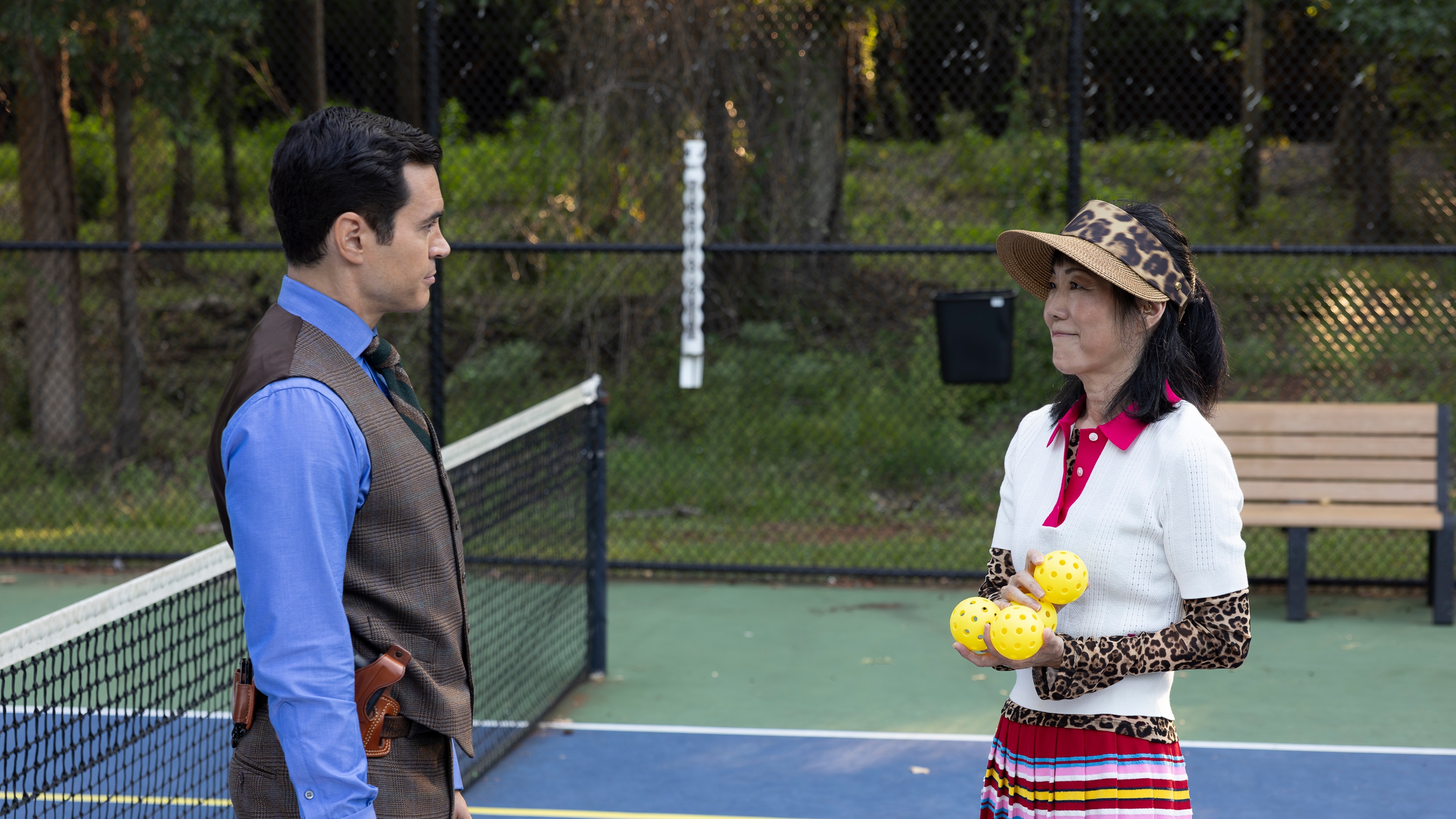 Will Trent (Ram&amp;oacute;n Rodriguez) and Dr. Roach (Margaret Cho) on a pickleball court. Will is looking at Dr. Roach who is holding yellow pickleballs and smiling at him.