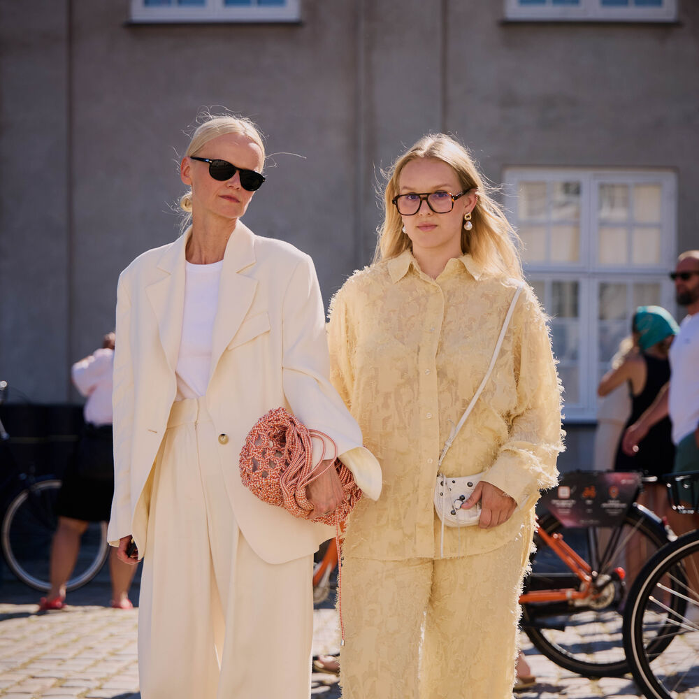 Two women pose. One wearing an all white suit and one wearing a yellow set. 