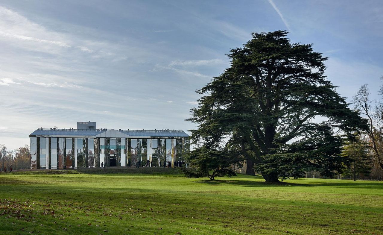 Contemporary château with polished steel mirrored exterior, with a large lawned area and towering cedar tree. 