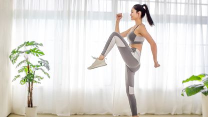 Woman raising her knee high as she completes a home workout