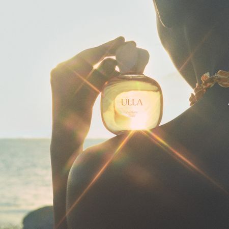 Woman in sun holding ulla johnson perfume bottle on shoulder 
