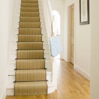 Golden brown floor leading to white stair case with golden stair case runner with golden stair case rods