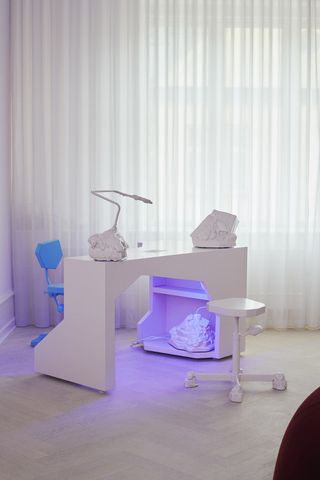 White curtain serving as backdrop to white desk with fluorescent purple light