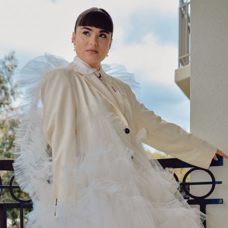 Devery Jacobs stands on a balcony wearing a white suit for the 2024 Emmys