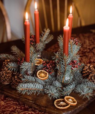 Christmas table decor with red candles, evergreen branches and pine cones