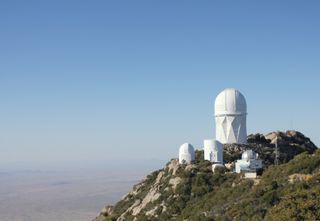 photograph of kitt peak national observatory high on a mountain with a blue sky above.
