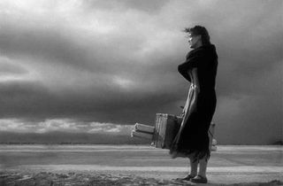 Black and white image of woman holding baggage by the sea shore