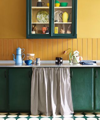 Yellow kitchen walls with jade green units and wall cabinet, fabric skirt in ticking fabric, white and green floor tiles, stainless steel countertop,