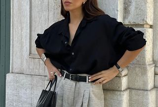 Woman in black button-down and gray trousers.