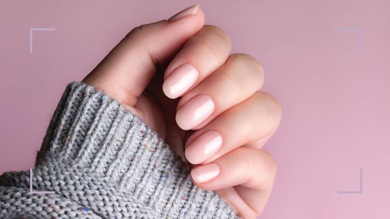 A woman's hand with biab nails treatment in a grey jumper on a dusky pinkbackdrop