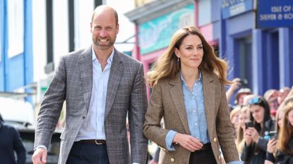 Prince William and Kate Middleton smiling as they walk past crowds