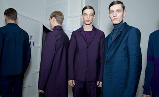 Four male models wearing looks from Jil Sander's collection. They are wearing purple and blue tops, turtle neck jumpers and textured suits and jackets
