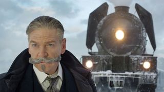 Kenneth Branagh's Poirot stares at something off screen as he stands in front of a train in Murder on the Orient Express