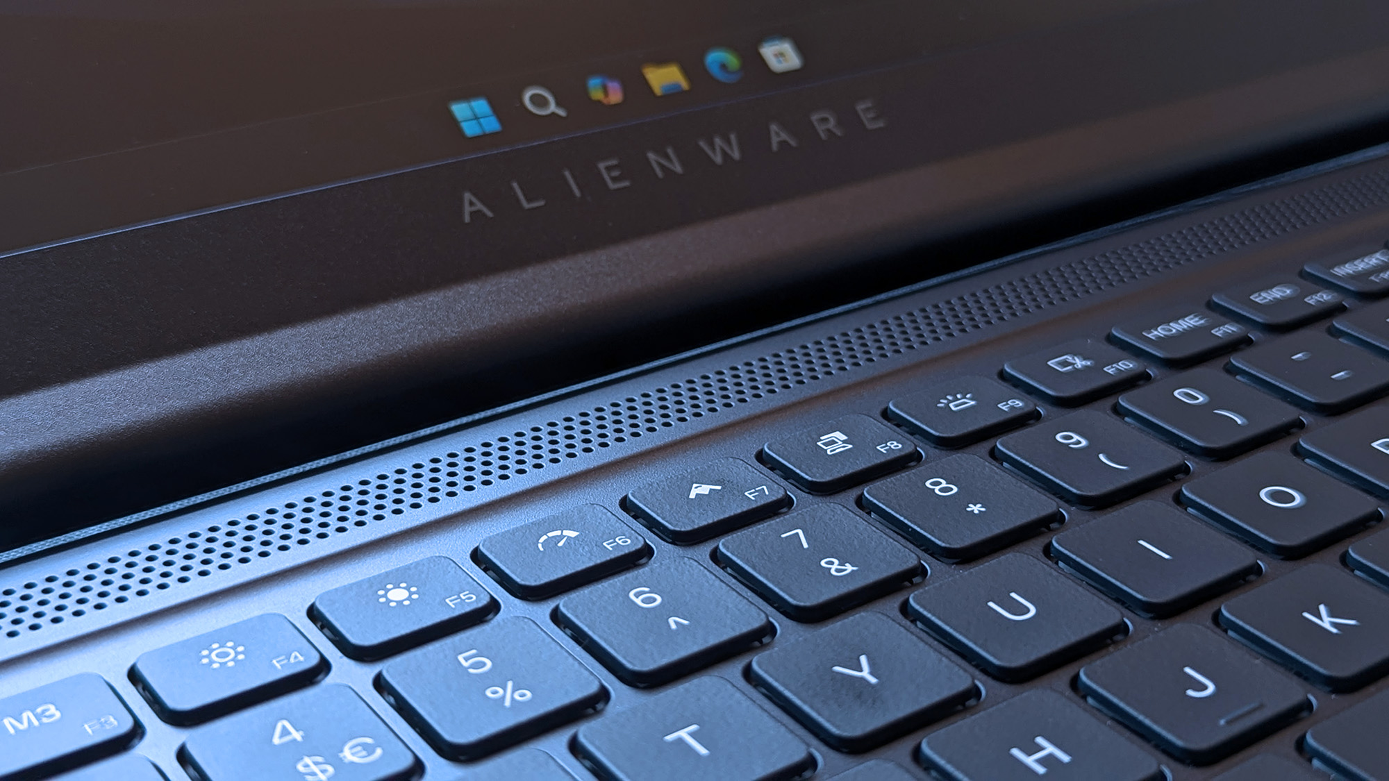 A close-up of an Alienware laptop shows the &amp;ldquo;ALIENWARE&amp;rdquo; branding above the keyboard, with visible function keys, number keys, and part of the Windows taskbar on the screen.
