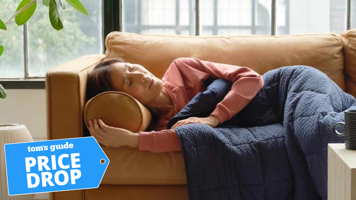 Woman lying down on the sofa on her side with a blue weighted blanket over her