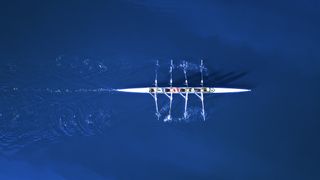 An aerial view of a team of rowers in a boat on classic blue water
