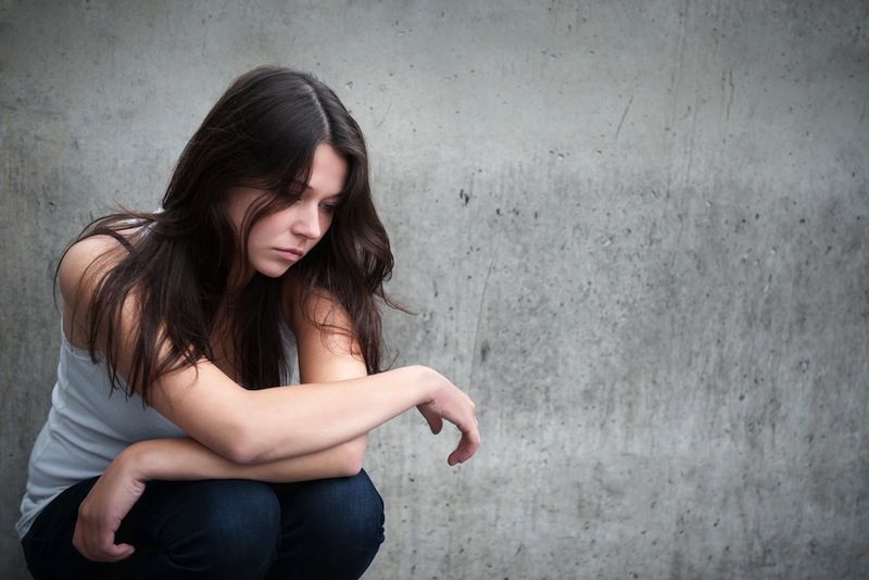 A teenage girl sits looking unhappy