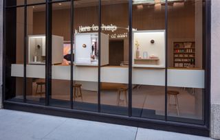 The Google store's façade featuring tall windows for a peek inside, where a desk with ‘here to help’ written in neon can be seen
