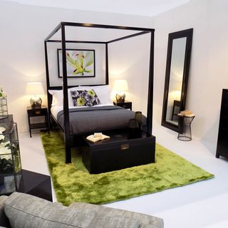 A white bedroom furnished with a modern, black four poster bed and a lime green rug